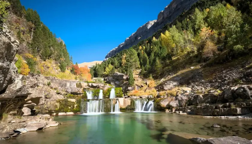 Cascada en un valle montañoso con árboles otoñales. Un lugar perfecto para rutas de senderismo inolvidables.