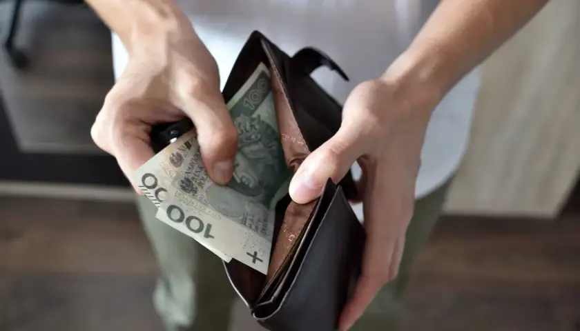 Ręce wkładają polskie banknoty 100 zł do portfela. Czy to wystarczy na świadczenia z MOPS dla niepełnosprawnych?