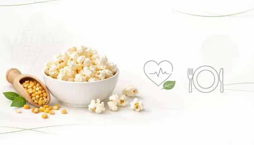 Miseczka popcornu, obok drewniana łyżka z ziarnami kukurydzy. Ikony serca z liściem i talerza z sztućcami sugerują zdrowe przekąski i ich popcorn kcal.