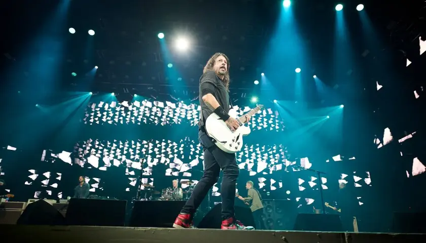 Dave Grohl z Foo Fighters gra na gitarze podczas koncertu, oświetlony niebieskimi światłami. Chce pokazać, jak grać.