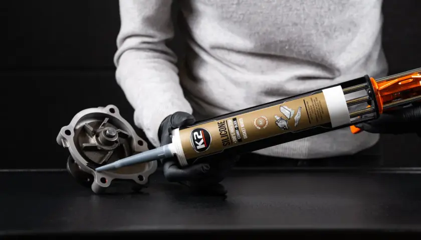 Rękawiczki i pistolet z czarnym silikonem K2. Aplikacja uszczelniacza na element pompy wodnej. Dowiedz się, jak długo schnie silikon.