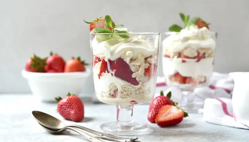 Pyszny Eton Mess z truskawkami i bitą śmietaną w kieliszkach, ozdobiony miętą.