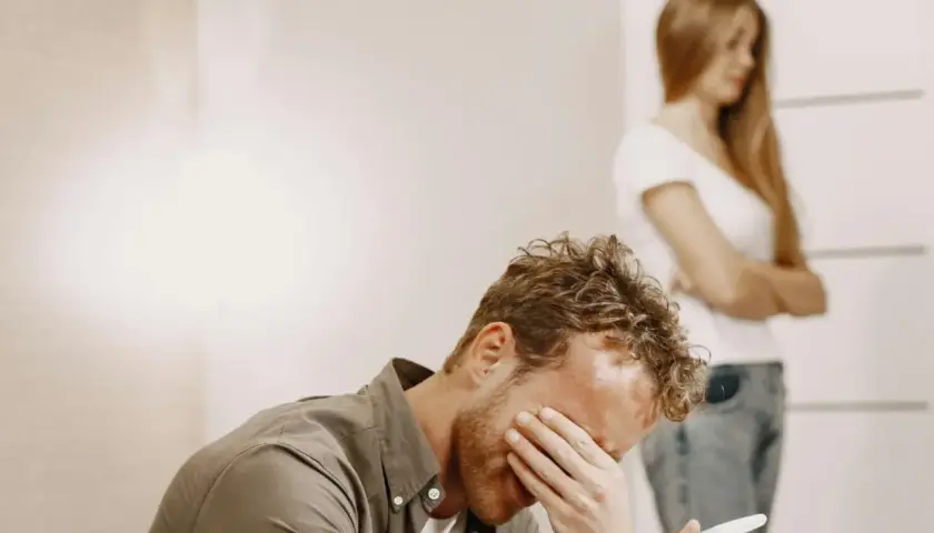 Uomo disperato con test di gravidanza in mano, mentre una donna si volta. Un esempio di uomini che non sanno stare in una relazione.