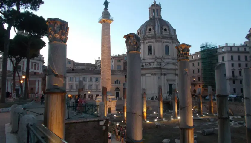 Antiche colonne onorarie illuminate di sera, con una cupola sullo sfondo.