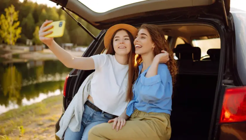 Dwie przyjaciółki robią sobie selfie przy samochodzie nad jeziorem. Idealny weekend z przyjaciółką!