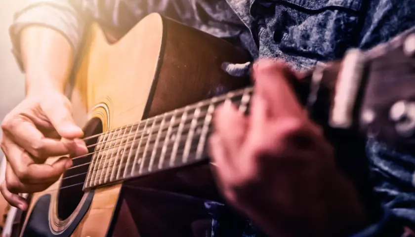 Ręce grające na gitarze akustycznej. Dowiedz się, jak samemu nauczyć się grać na gitarze, ćwicząc akordy i rytm.