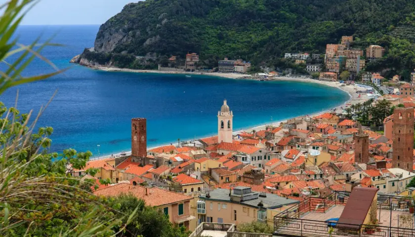Vue d'un village pittoresque sur la côte de l'Italian Riviera, avec des maisons aux toits rouges, une plage de sable et une mer bleue étincelante.