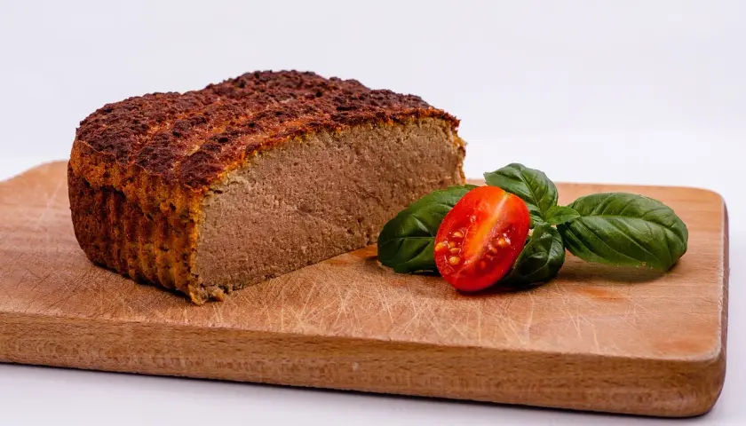 Pokrojony pasztet na desce z pomidorkiem koktajlowym i bazylią.