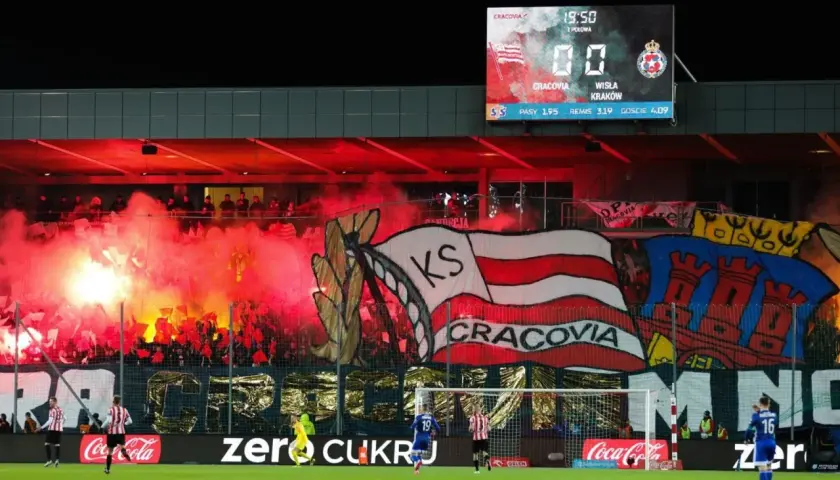Oprawa kibiców najstarszego klubu piłkarskiego w Polsce, Cracovii, z racami i transparentami. Na tablicy wyników 0:0.