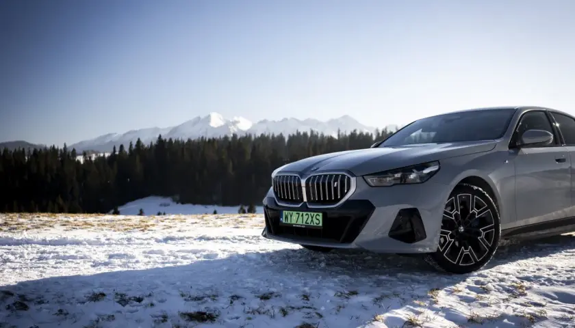 Szare BMW i5 na tle ośnieżonych gór i lasu.