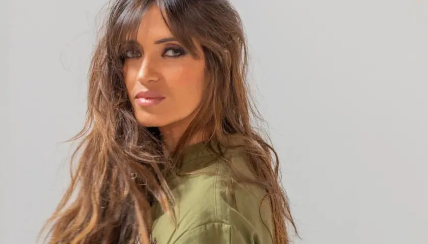 Mujer con cabello castaño largo y ondulado, con flequillo cortina que enmarca su rostro.