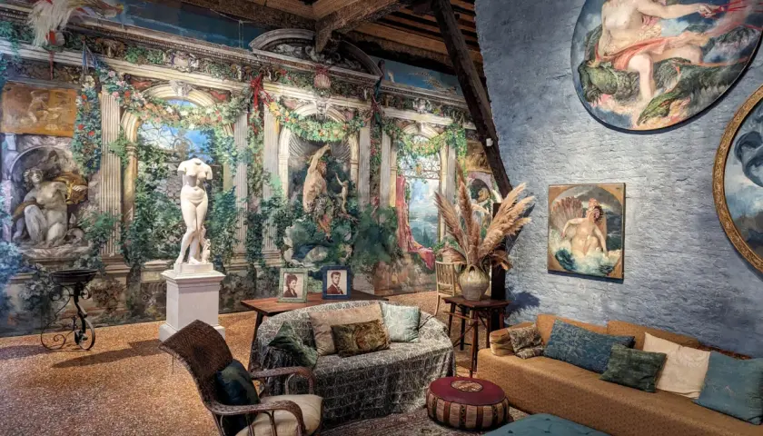 Intérieur du museo Fortuny, avec une statue antique, des peintures murales luxuriantes et des meubles confortables.