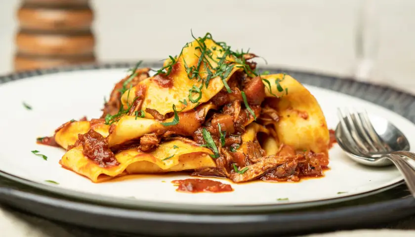 Herzhaftes Pasta Ragu mit breiten Nudeln, übergossen mit einer reichhaltigen Fleischsauce und garniert mit frischen Kräutern.