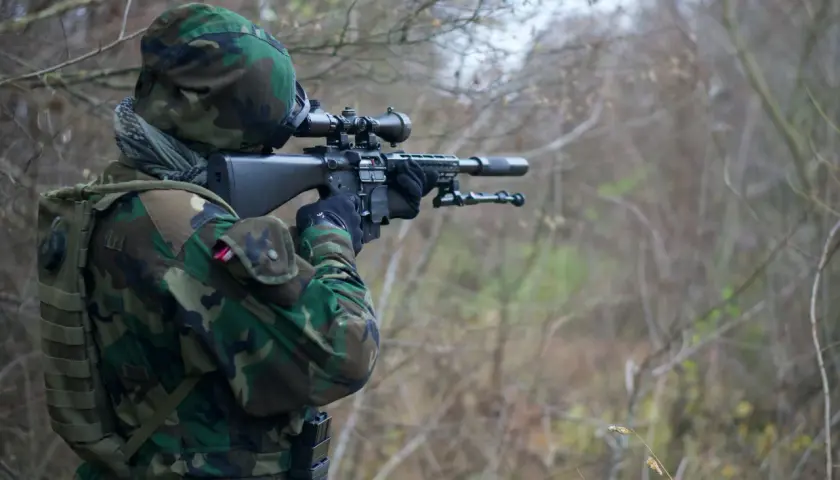 Żołnierz w kamuflażu celuje z karabinu snajperskiego. Widać lunetę, przez którą obserwuje cel, a zjawisko paralaksy w lunecie jest kluczowe dla precyzyjnego strzału.