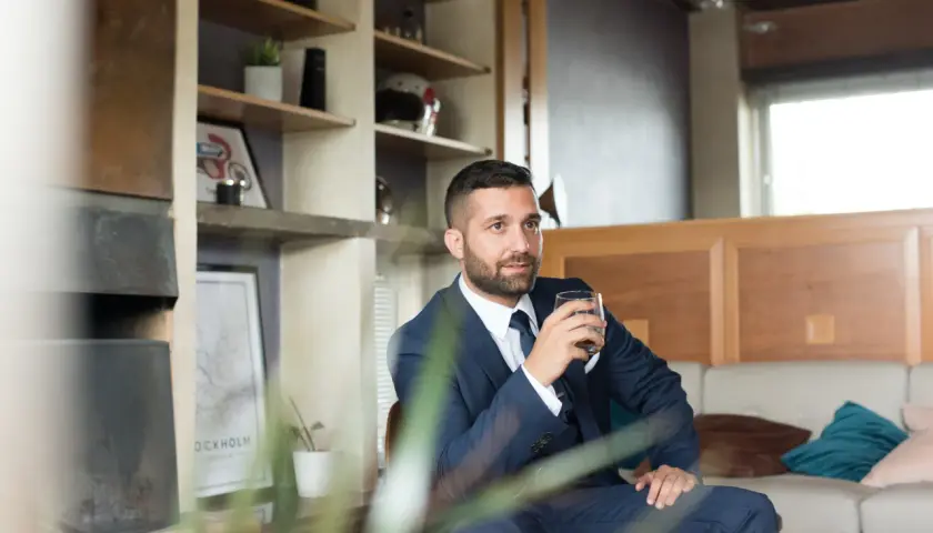 Elegancki mężczyzna w garniturze, z drinkiem w dłoni, emanuje spokojem i pewnością siebie w towarzystwie.