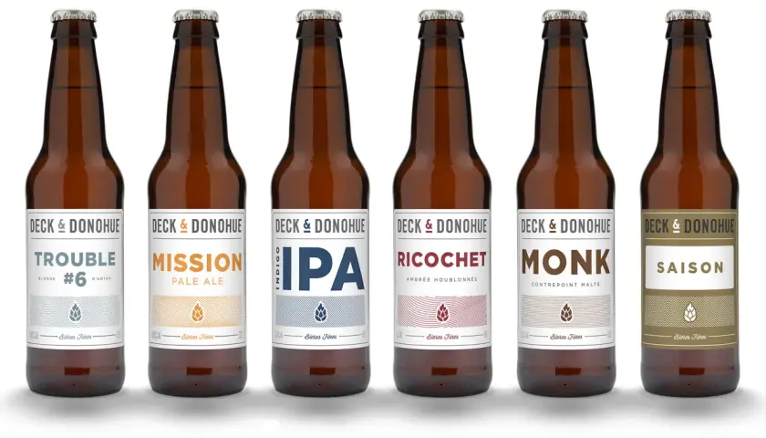 Six bouteilles de bière de la marque Deck & Donohue, proposant différents types de bière : Trouble, Mission, IPA, Ricochet, Monk et Saison.