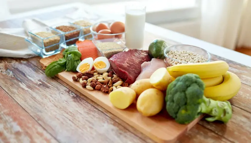 Deska z różnorodnymi produktami spożywczymi: mięso, ryba, jajka, orzechy, warzywa, owoce, mleko i ziarna.