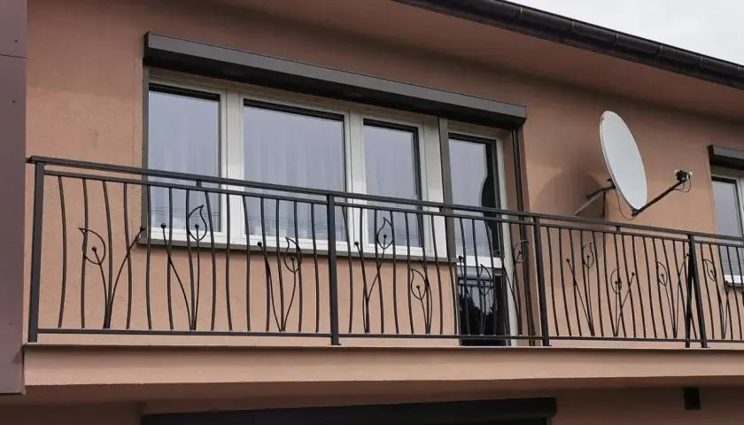 Elegancka, czyszczenie balustrady metalowej z motywem roślinnym. W tle okna i antena satelitarna.