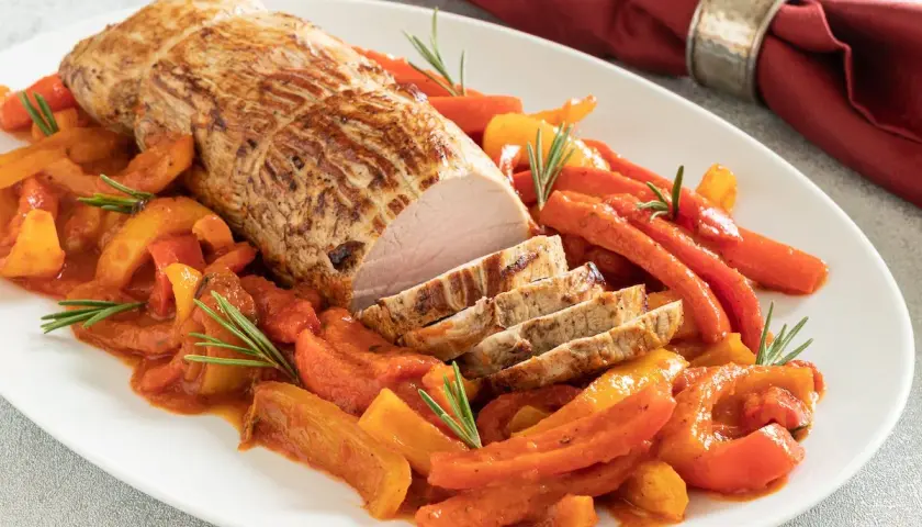 Arrosto di vitello in pentola con peperoni e carote, guarnito con rosmarino. Un piatto succulento e colorato.