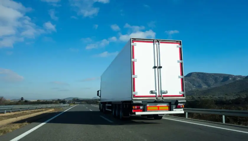 Biała naczepa ciężarówki na autostradzie, przewożąca fracht. Co to jest fracht? To towar w transporcie.