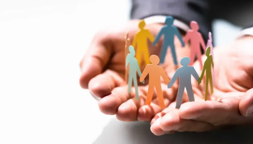 Hands cradle colorful paper people, symbolizing the benefits of equality, diversity, and inclusion in the workplace.