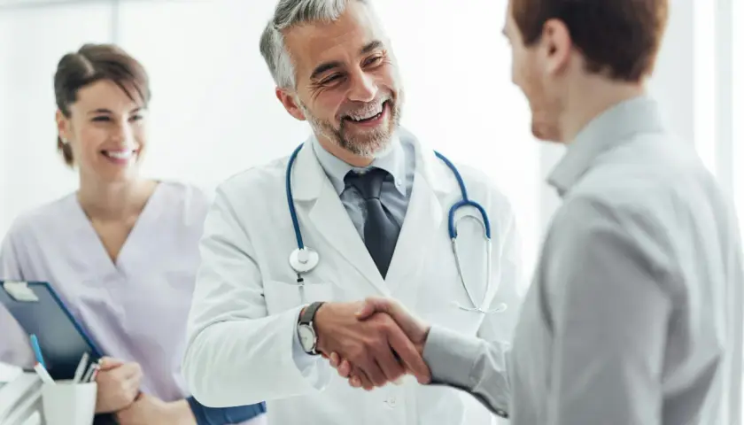 Ein Arzt schüttelt einem Patienten die Hand, ein Lächeln der Zufriedenheit. Im Hintergrund eine lächelnde Krankenschwester. Ein schönes Bild für eine Danksagung Krankenhaus.