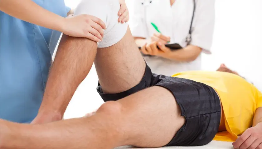Fizjoterapeuta bada kolano pacjenta po urazie, być może zerwaniu acl. Lekarz notuje.