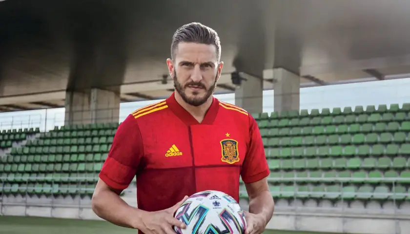 Piłkarz w czerwonej koszulce Hiszpanii z piłką, gotowy do gry w stylu tiki-taka.
