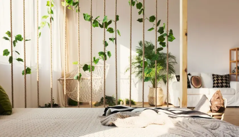 Grüne Ranken zieren Seile, die als Raumteiler Ideen zum Selbermachen dienen. Ein Hängesessel und Pflanzen schaffen Boho-Flair.