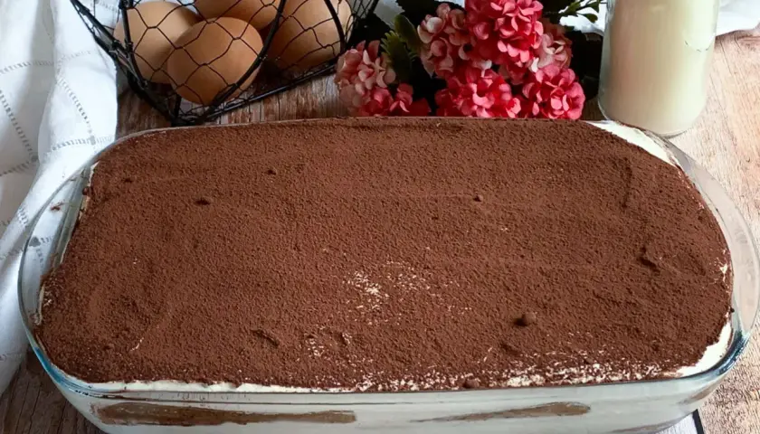 Tiramisù fatto in casa, una ricetta con panna che promette golosità. Uova fresche e cacao in polvere completano la scena.