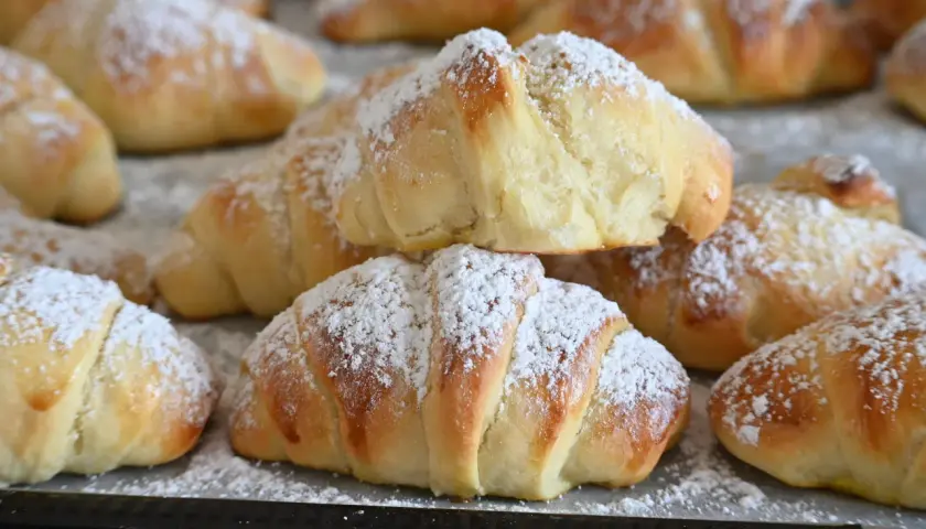 Brioches fatte in casa, dorate e soffici, cosparse di zucchero a velo. Un dolce profumo che invita a gustare la colazione.