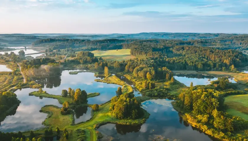 Malowniczy litewski krajobraz z licznymi jeziorami, lasami i zielonymi polami o wschodzie słońca.