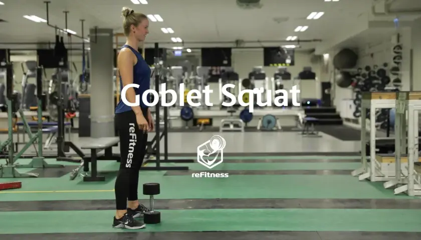 Kvinna förbereder sig för en goblet squat med en hantel i ett gym.