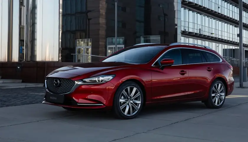 Czerwona Mazda 6 kombi na tle nowoczesnego budynku. Poznaj jej imponujące mazda 6 wymiary i styl.