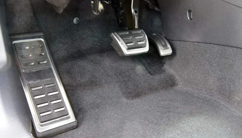 Widok na pedały w samochodzie: sprzęgło, gaz i hamulec. Po lewej pedał podparcia stopy, pośrodku gaz, a po prawej hamulec.