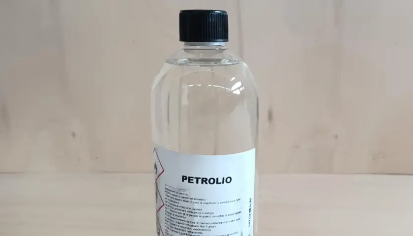 Bottiglia di **petrolio bianco su legno**. Liquido infiammabile, da usare con cautela.