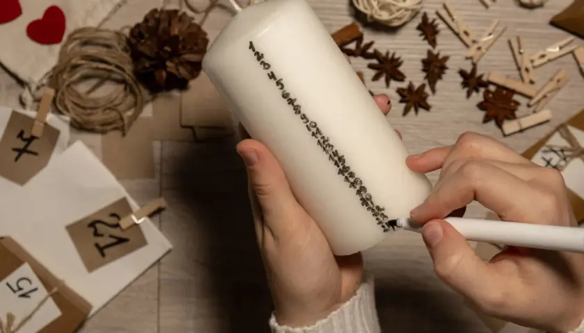 Hände beschriften eine Kerze mit Zahlen für einen Adventskalender. So lassen sich Adventskalender Geschenke selber machen.