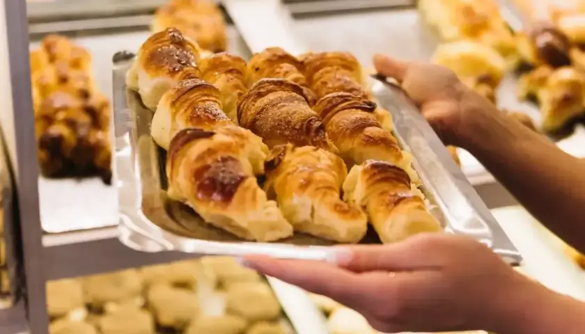 Taca z croissantami, którą trzymają ręce, na tle innych wypieków.