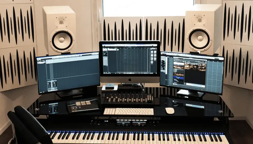 Configuration home studio avec trois écrans, enceintes, clavier maître et console de mixage.