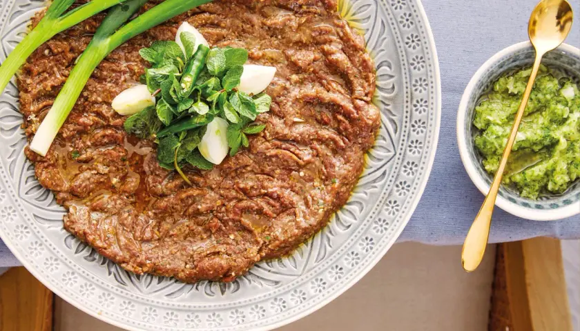 En tallrik med kibbeh nayyeh, rå köttfärs kryddad med bulgur och örter, toppad med vitlök, mynta och chili. Serveras med en grön sås.