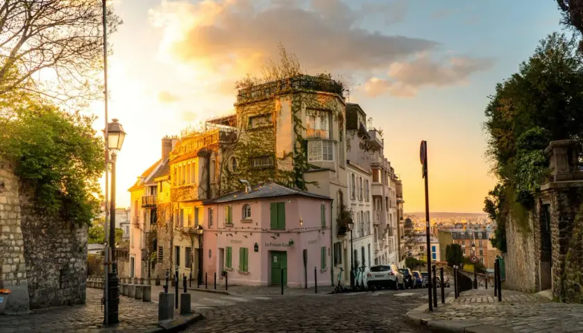 Urokliwa uliczka Montmartre, idealna na spacer z **paryż przewodnik**. Zachodzące słońce oświetla kamienice i brukowaną drogę.