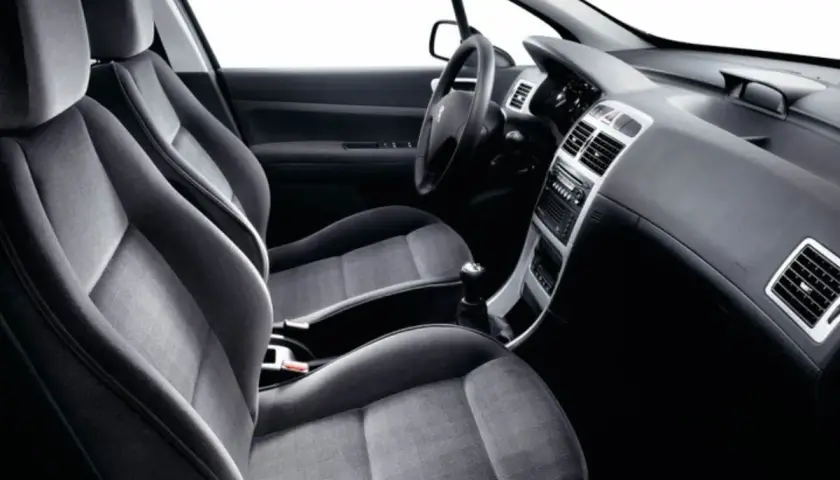 Interior de Peugeot 307, asientos delanteros de tela gris, salpicadero y consola central. Sin anomalia anticontaminacion visible.