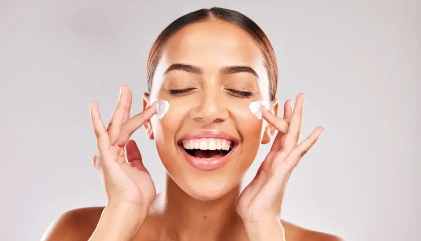 Mujer sonriente aplicándose crema en el rostro. Descubre para qué sirve la niacinamida en la piel y luce radiante.