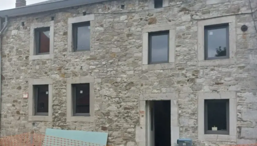Façade d'une maison en pierre, en cours d'isolation. Fenêtres neuves et entrée ouverte sur un chantier.