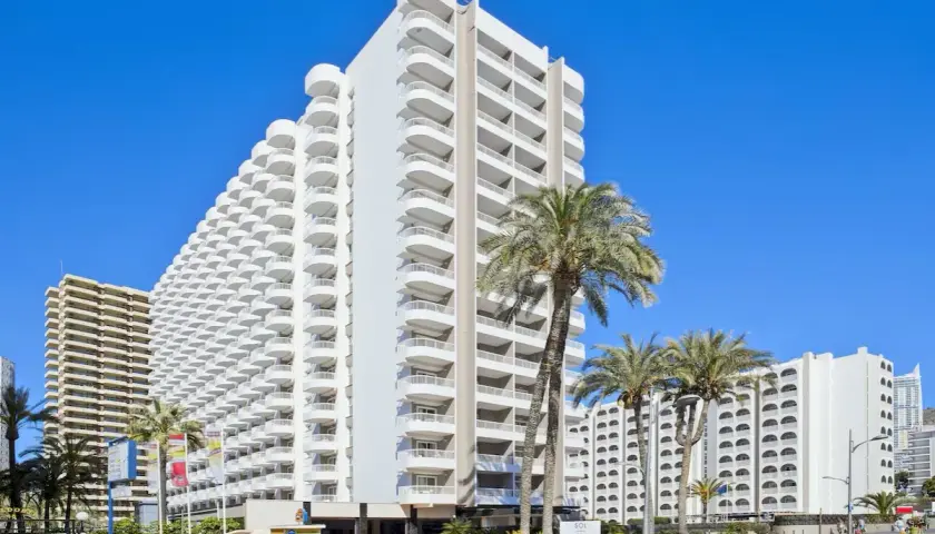 Edificio Sol con balcones curvos y palmeras bajo un cielo azul.