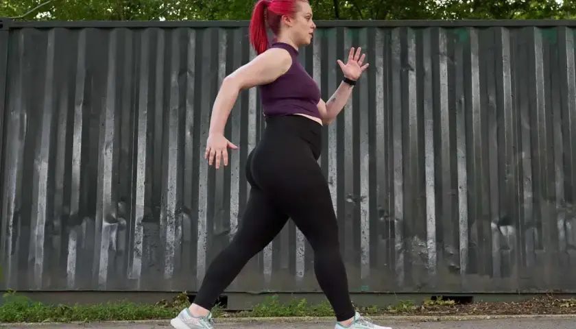 Kobieta z różowymi włosami w kucyku uprawia power walking przed szarym, pofałdowanym kontenerem.