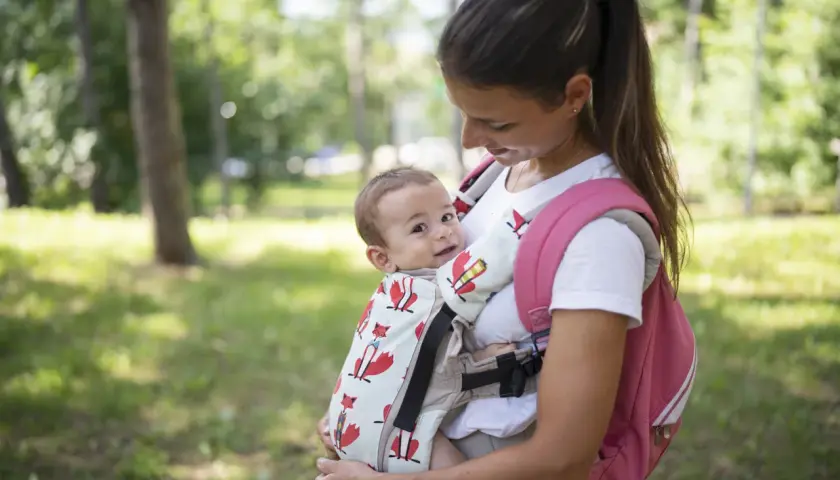 Uśmiechnięta mama z niemowlakiem w nosidełku z lisami. Fizjoterapeuta poleciłby takie, bo wspiera prawidłowy rozwój malucha.