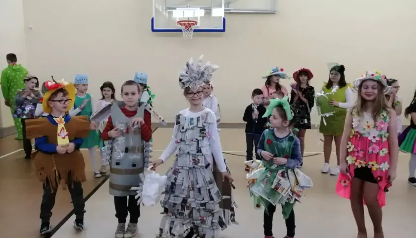 Dzieci prezentują stroje na Dzień Wiosny. Chłopiec w brązowym stroju z frędzlami, obok niego chłopiec w stroju z butelek.