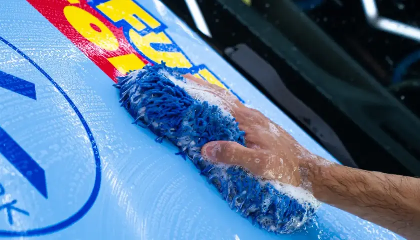 Mano con spugna blu insaponata mentre si lava un'auto con adesivi gialli e rossi.