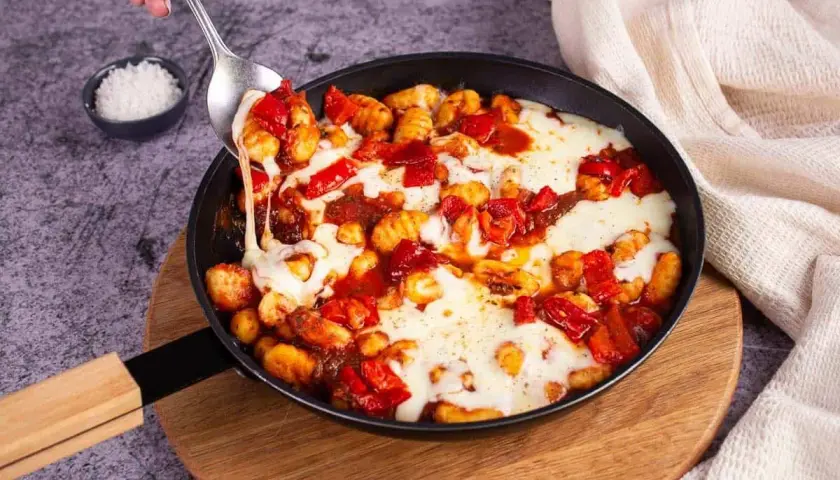 Gnocchis tomate mozza fondants, servis dans une poêle, avec une cuillère qui en prélève une portion filante.